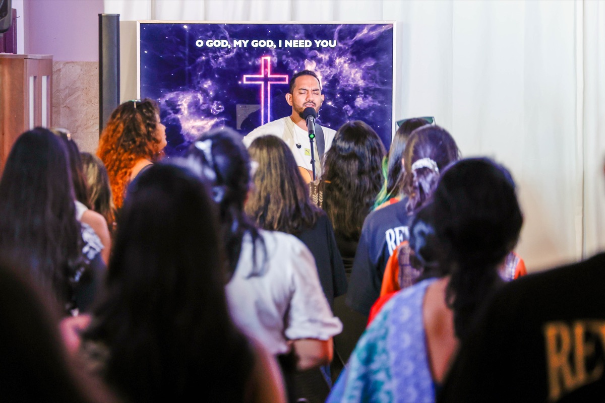 Worship leader singing before the congregation with a glowing cross on screen behind him